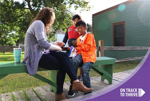 Two students sitting on a bench outside smiling with their teacher